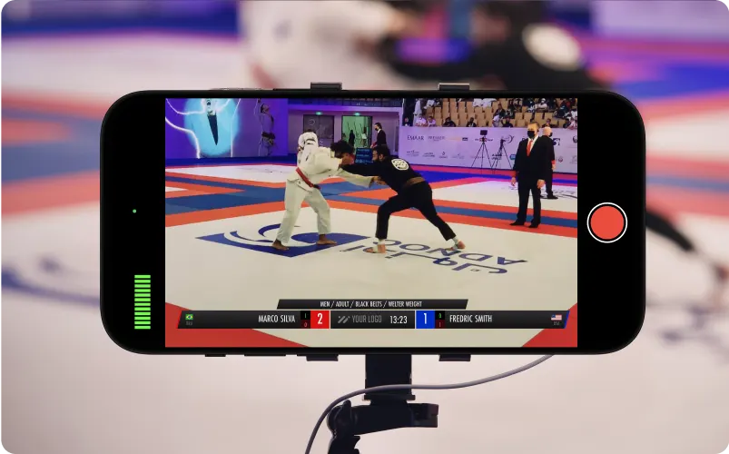 A smartphone on a tripod streaming a match on the mat